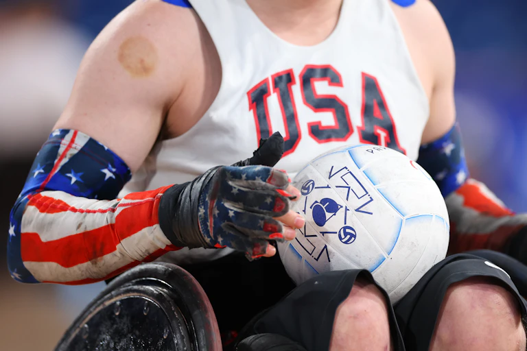 Close-up of young man sitting in wheelchair holding a ball while wearing a white pinny that reads 'USA.'