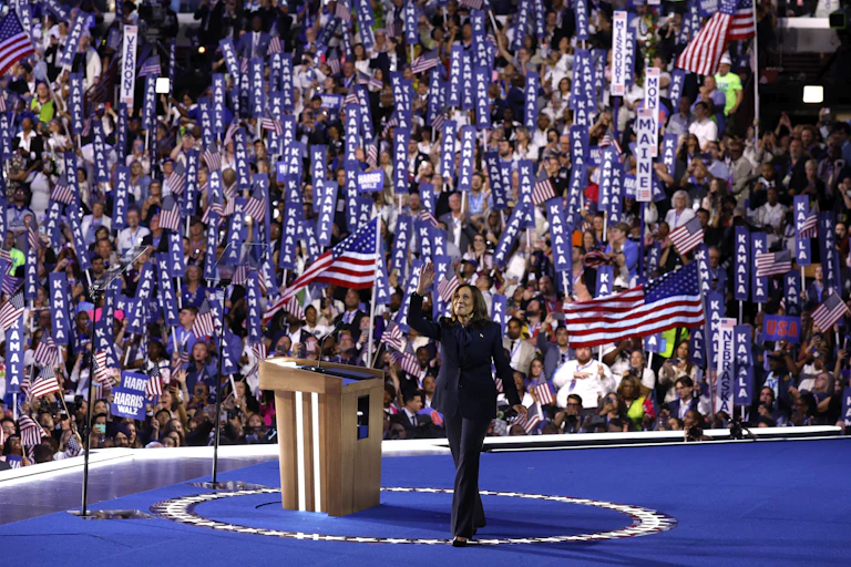 A woman in a dark blue suit waving to a large crowd from a stage.