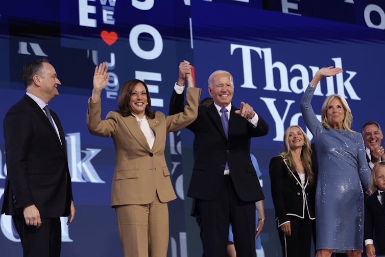 Four people standing on a stage, smiling and waving.