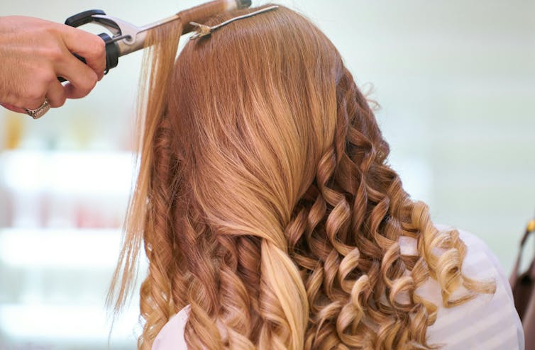 A woman gets her hair curled and it forms into ringlets.