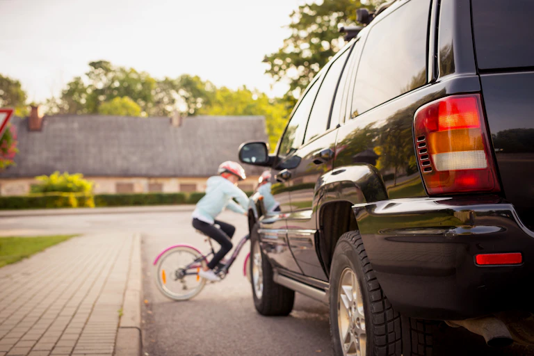 A young girl on a bicycle rides onto the road in front of a car