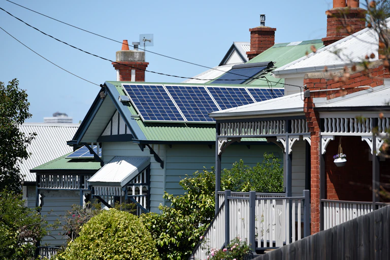 Houses in a street sit in the sunlight, there are power lines connecting the homes to the electricity poles.