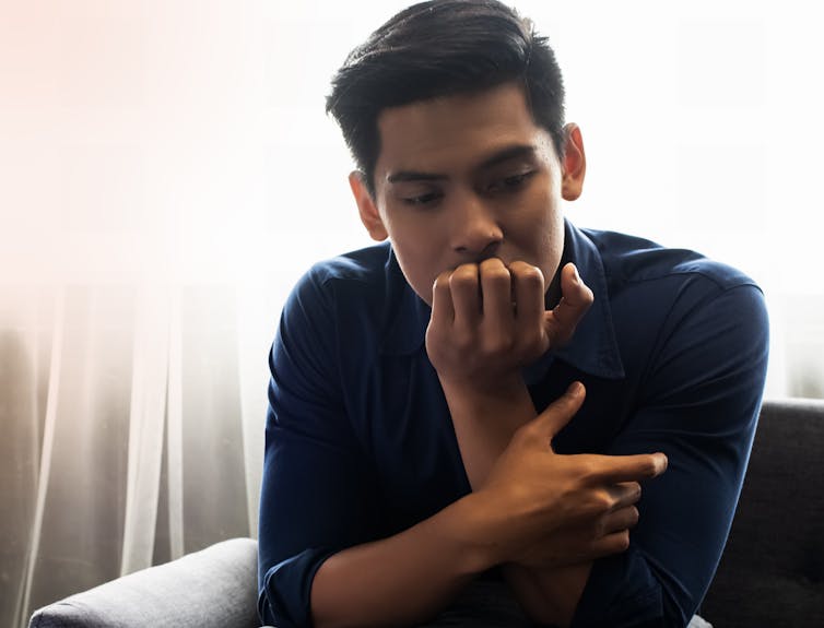 A young man seated on a couch appears pensive.