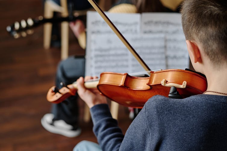 A young person plays the violin in a string ensemble.