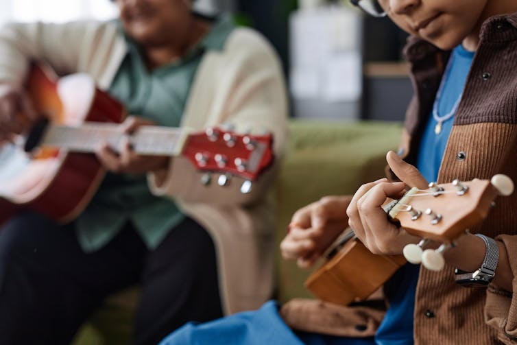 An adult plays guitar next to a child on the ukulele.