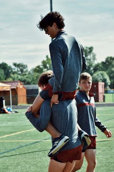 A teenage boy carries another on his shoulders while a friend looks on.