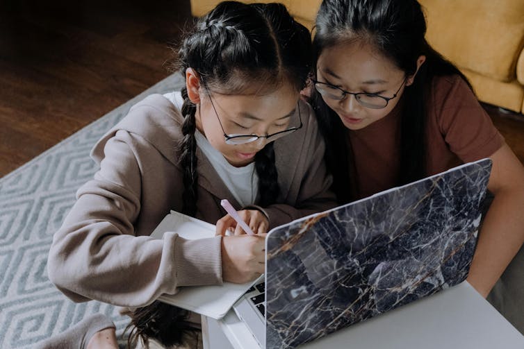 Two teenage girls wearing glasses lean over a laptop.