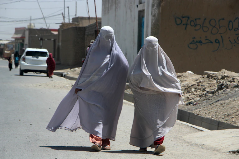 Two Afghan women covered from head to foot in the Islamic hijab, walking down the street in Kandahar, Afghanistan, August 2024.
