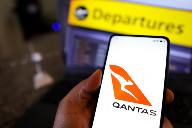 qantas app on a mobile screen in front of an airport departures board