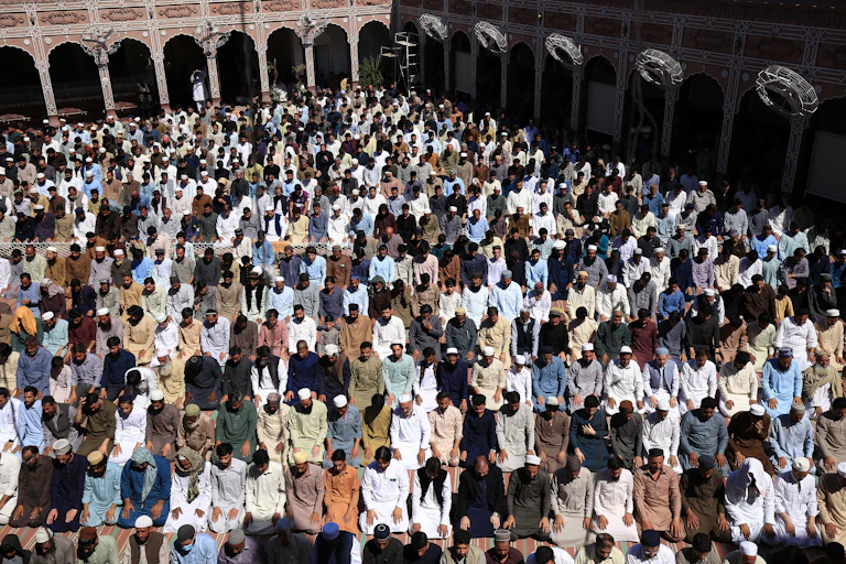 Overhead view of a large crowd of Muslim men gathering in a square for prayer, kneeling side by side in rows