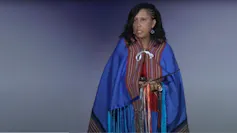 A woman wearing blue robes stands in front of a mic.