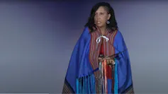 A woman wearing blue robes stands in front of a mic.