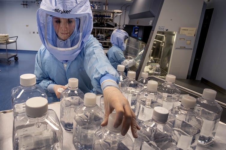 woman fully contained in personal protective gear reaches across glass bottles