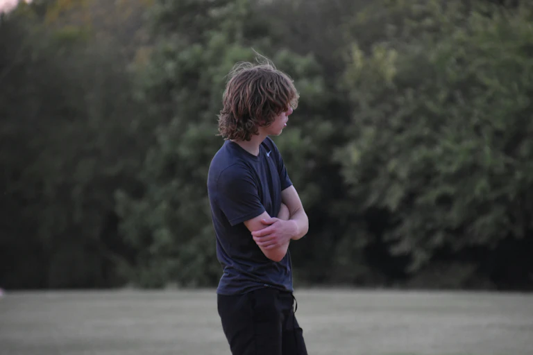 A moody teenage boy, in T-shirt and jeans, arms crossed.