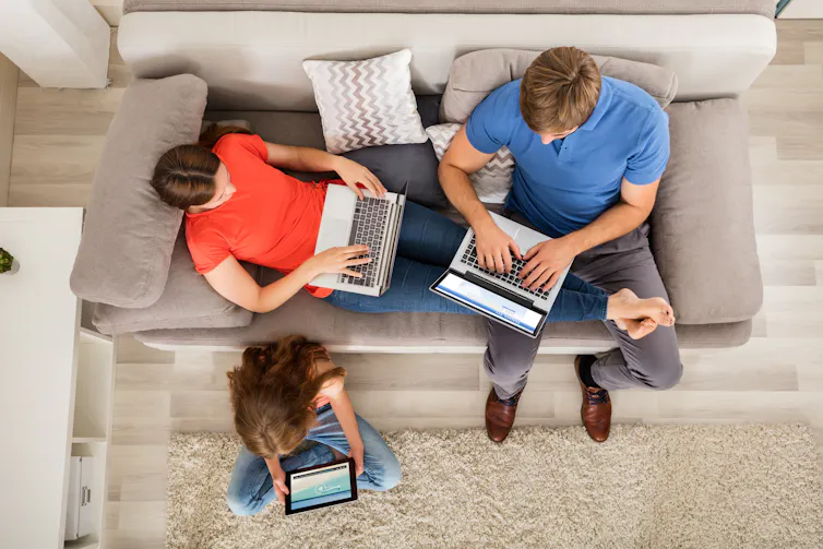 Husband and wife using laptops, child using tablet