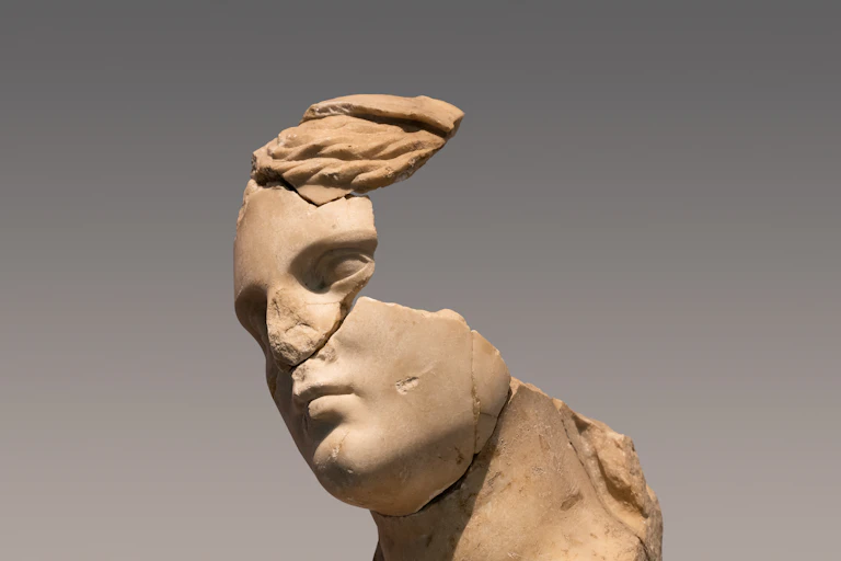 A largely damaged ancient statue head of a woman with pieces missing.
