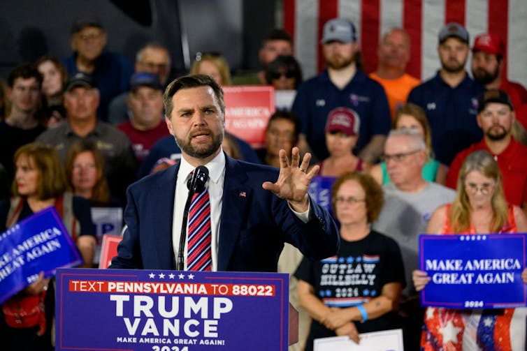 A man with a beard speaks at a podium.