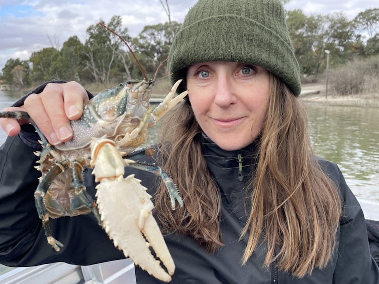 A woman with long brown hair wearing a green beanie holds one of the Murray crayfish prior to release.