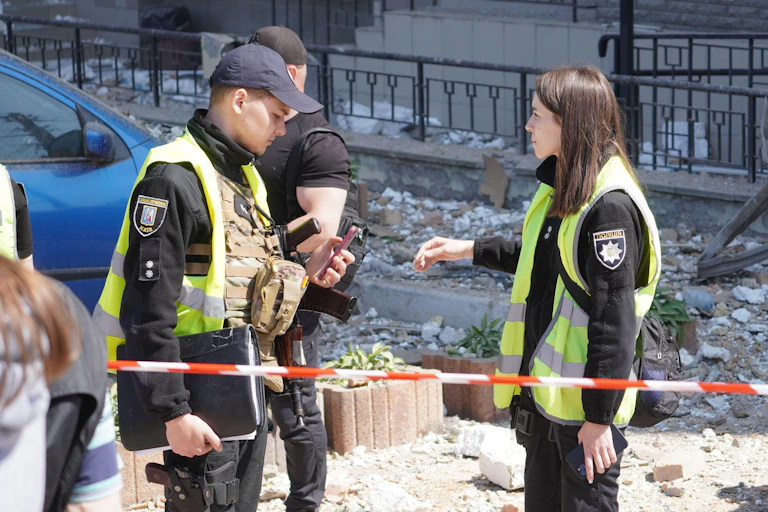 Two officials in high viz jackets surveying bomb damage.