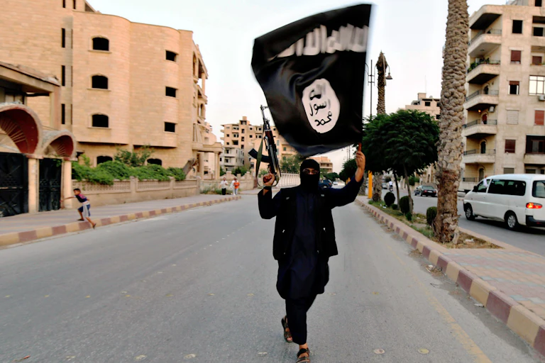 An Islamic State fighter holding a gun in the air in one hand and a black flag in the other.