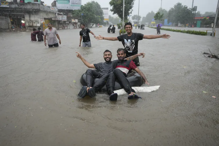 A group of young men pose with an inner tube in a flooded street.