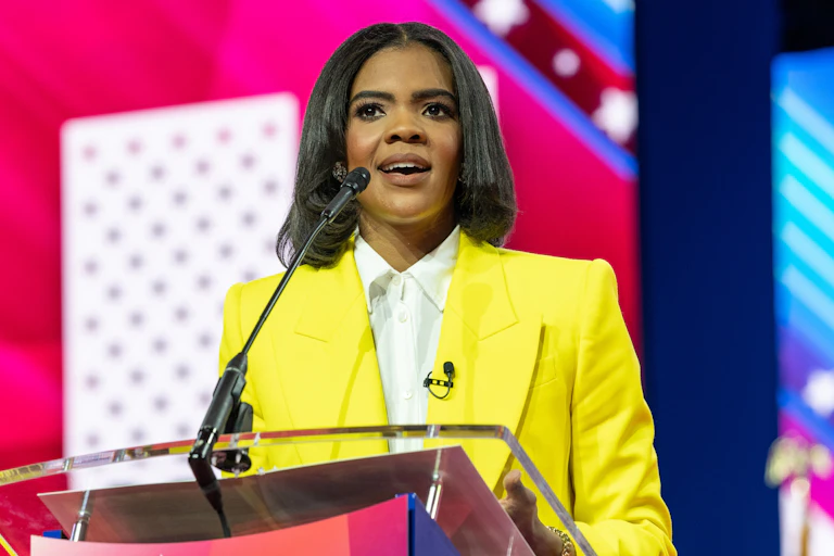 A woman in a bright yellow blazer speaks at a lectern