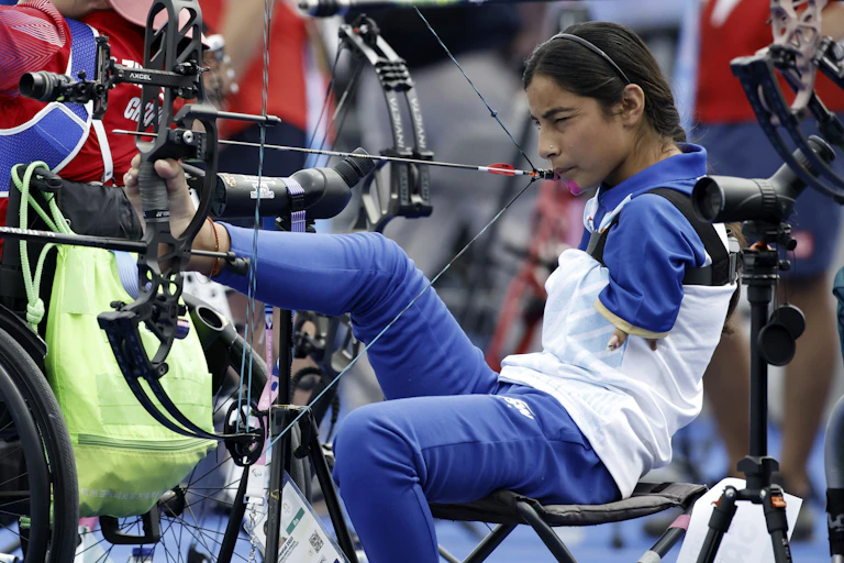 Para athlete competes in archery event, holding bow with her foot and arrow with her mouth