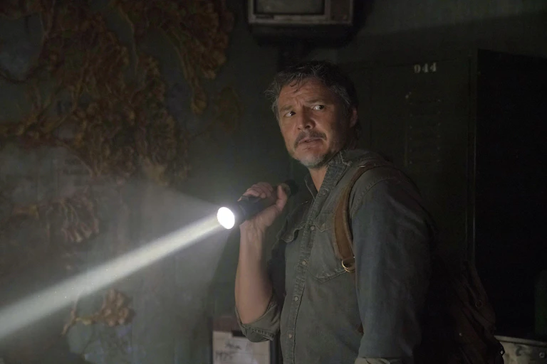 A man shining a torch in a darkened room while looking over his hsoulder nervously.