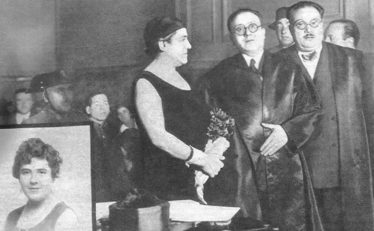 Una mujer de pie al lado de dos hombres junto al retrato de otra mujer más joven.