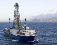 A boat with a large derrick, moving away from land