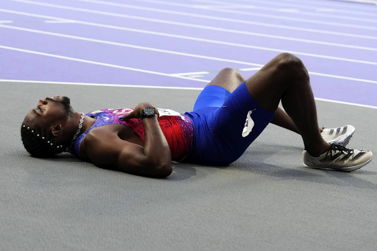 A man in athletic clothing lying on the ground beside a track