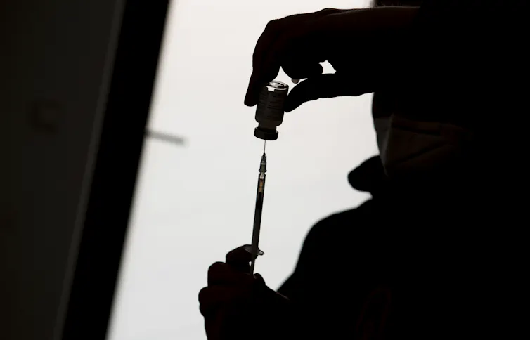 Silhouette d’une personne remplissant une seringue à partir d’un flacon de vaccin
