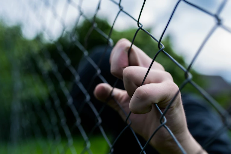 A young male hand grabs at a chicken wire fence