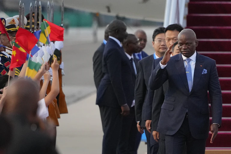 A man wearing a suit salutes a crowd as he gets off a plane.
