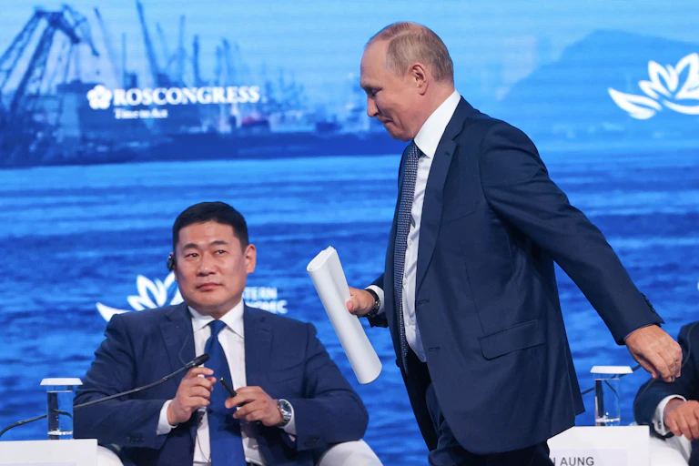 A man in a blue suit walks past a seated man.