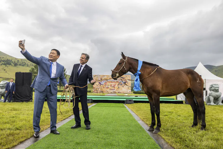 Two men in suits take a selfie photo with a horse.