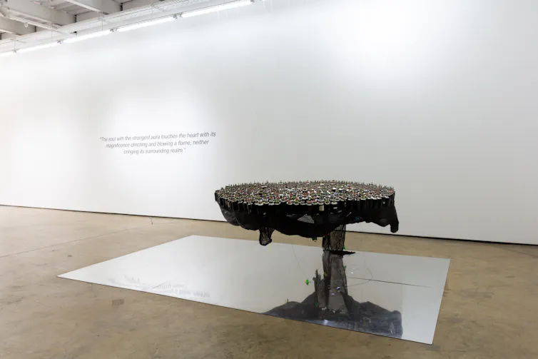 In the foreground, a sculpture suspended and made out of lanterns. In the background a poem stencilled on a white wall.