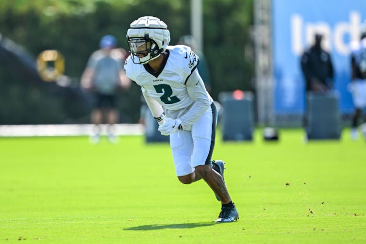 Young man runs while wearing a white and green football jersey and white helmet.
