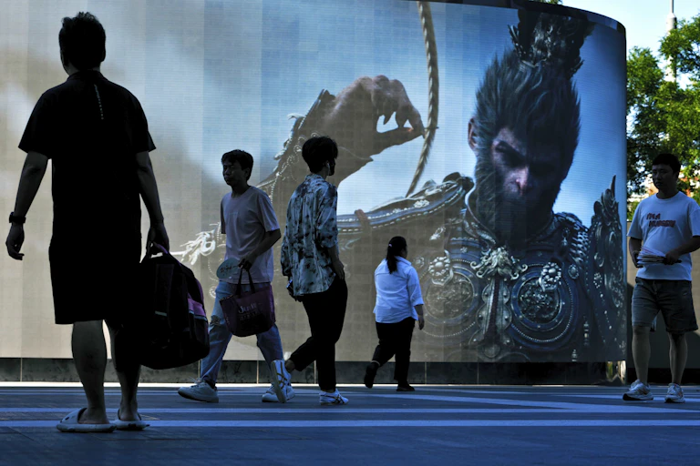 Photo of people walking past a large video billboard with a picture of a monkey in an elaborate suit of armour.