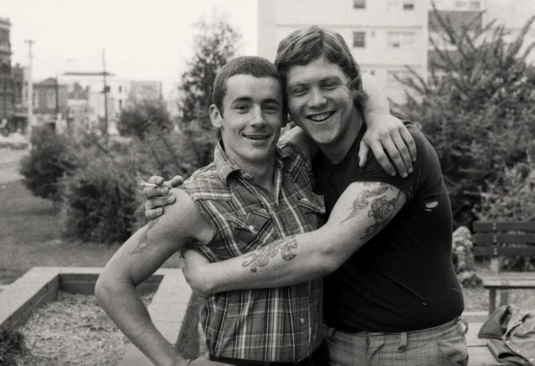 Two tattooed youths with Sharpie haircuts hug each other.