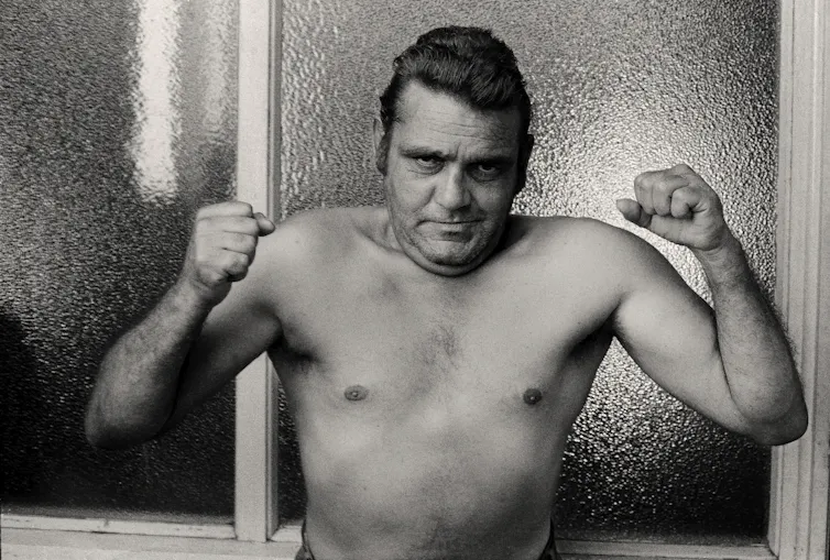 A shirtless man flexes his muscles.