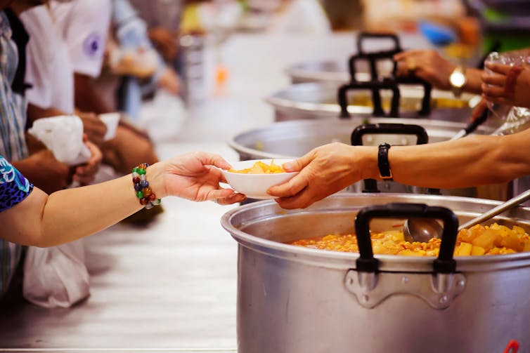 People standing behind large pots had bowls of food to other people.