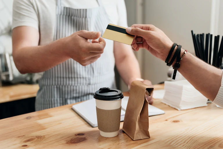 Man behind counter accepting payment for coffee by credit card