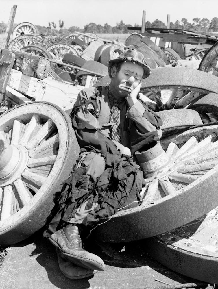 A clown rests on wagon wheels.