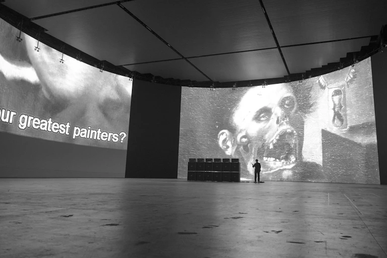 Two large screens show black and white digital imagery, with a small figure standing in front of one.