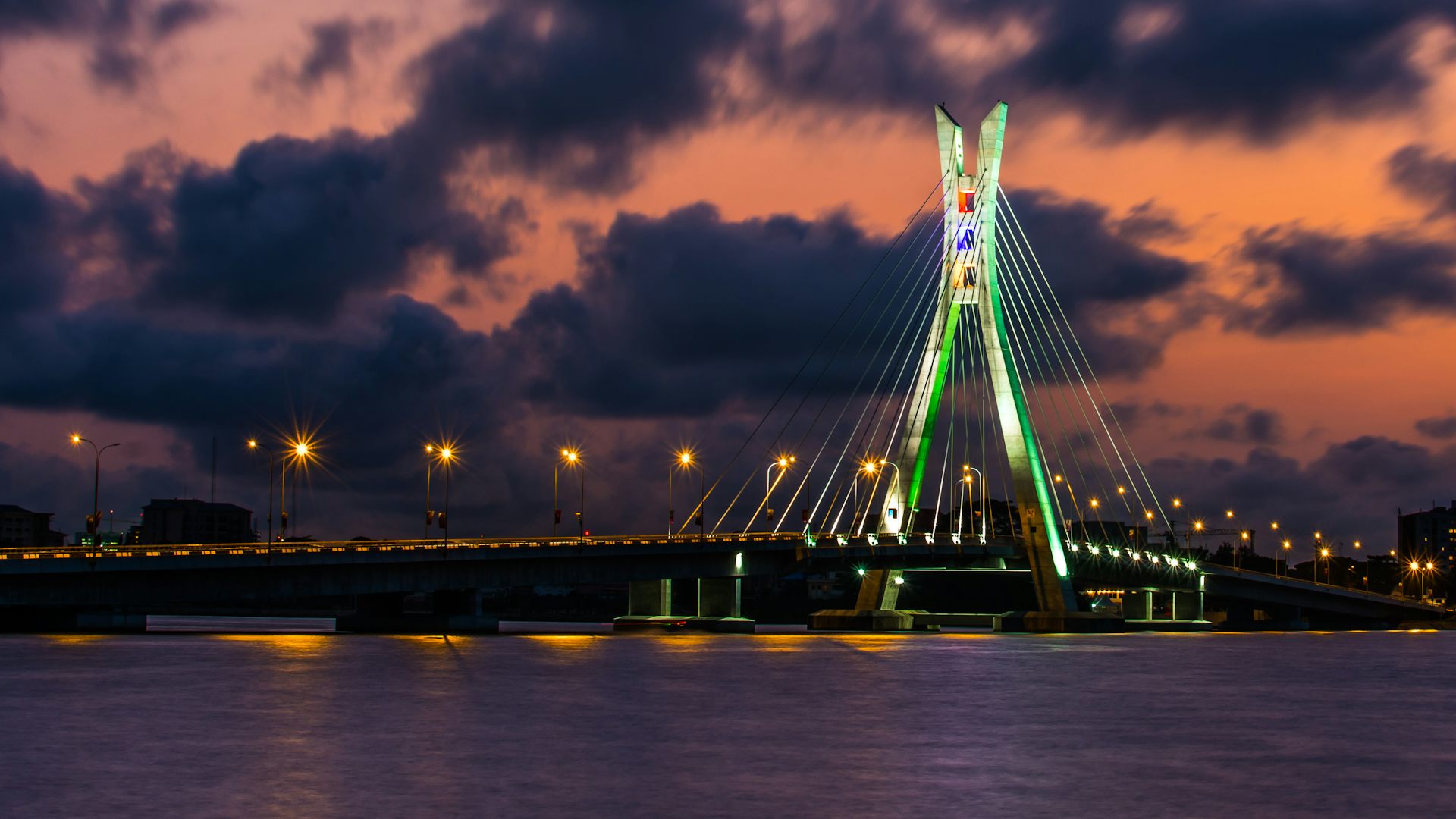 Lit-up bridge across water, against an evening sky
