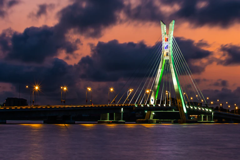 Lit-up bridge across water, against an evening sky