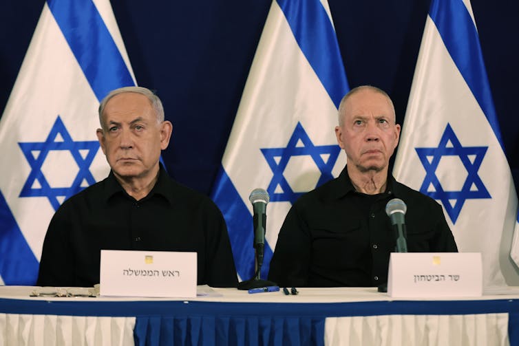 Benjamin Netanyahu and Yoav Gallant sat at a desk in front of Israel flags.