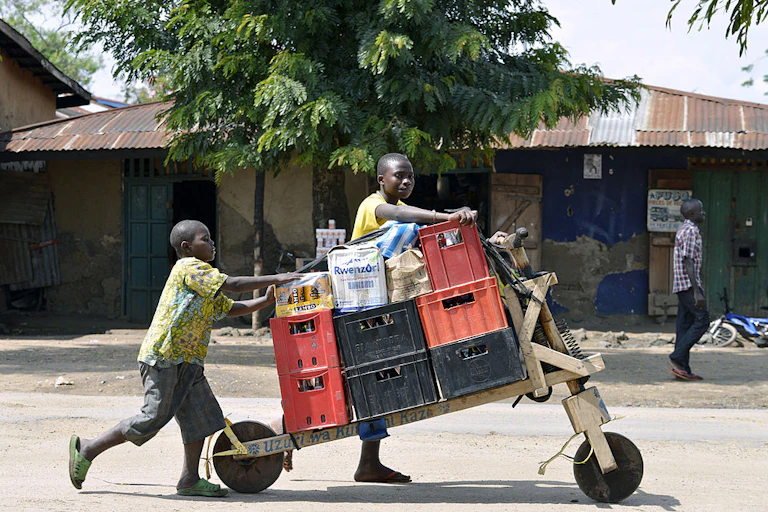 Congolese boys push a load on a two-wheeled cart through a town street.