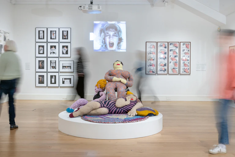 A scene from an art gallery with people (blurred by the camera) looking a t various works of art.
